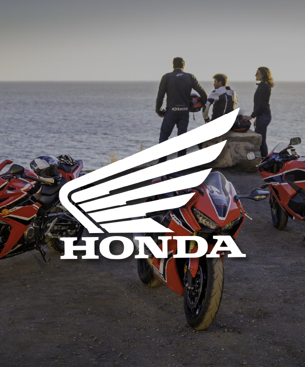 Honda logo overlayed on red sport motorcycles parked by the coast, with three people standing in the background.