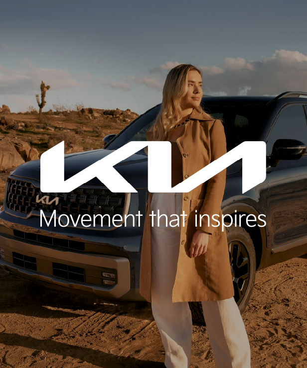 Kia logo with the slogan 'Movement that inspires' over a woman standing beside a black SUV in a desert landscape.