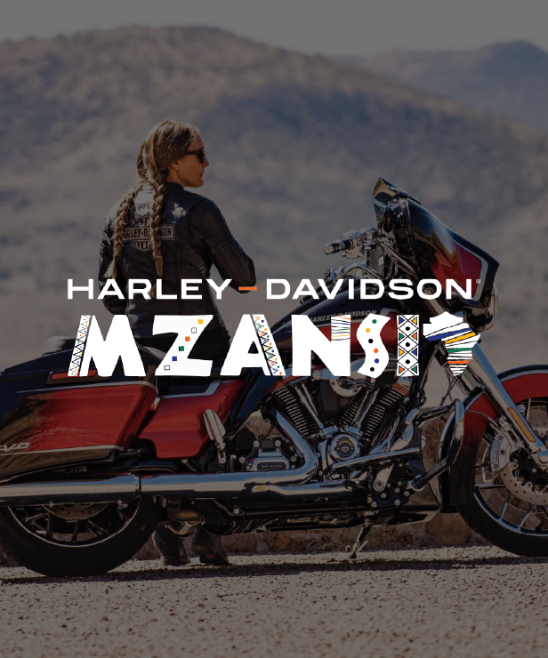 Biker in a leather jacket standing beside a red Harley‑Davidson motorcycle in a desert landscape, with bold HARLEY‑DAVIDSON MZANZI branding across the image.