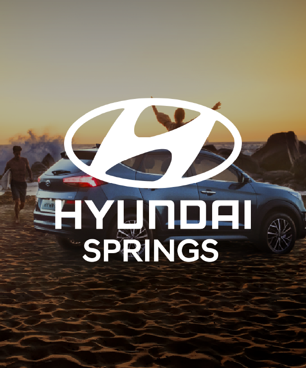 Hyundai logo and wordmark over a blue car parked on a sandy beach at sunset with people in the background.